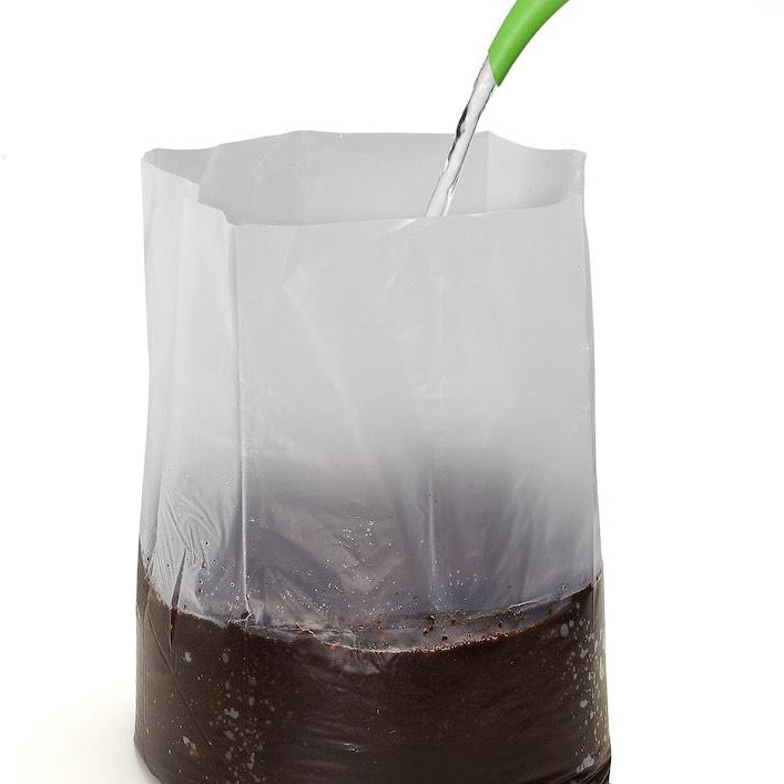 Soil being poured into a clear plastic container containing coco coir with a green tool on a white background