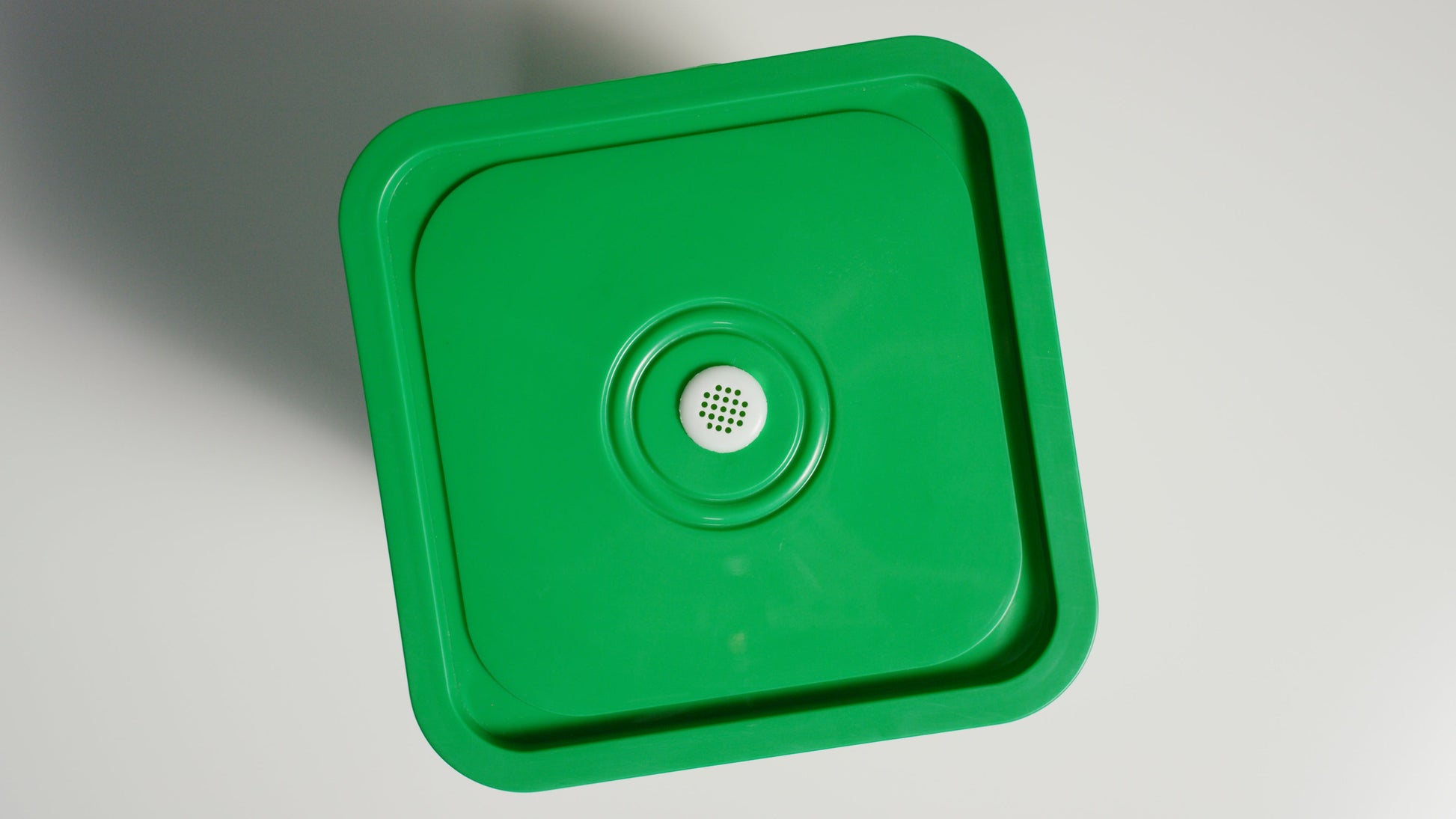 Green plastic lid on a Worm Bucket a gray background